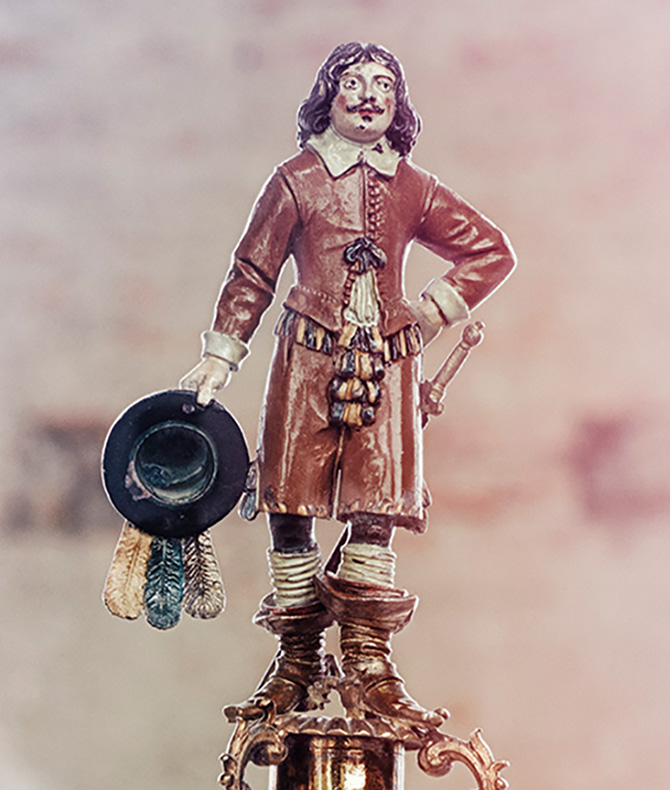 Close-up of the top decoration on the glass trophy, showing a man in 17th Century clothes.