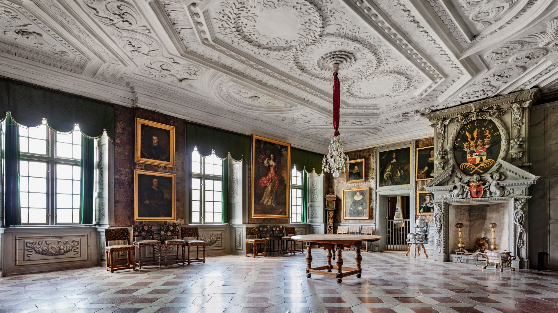  Great hall in the castle containing a fireplace with a coat of arms, oil paintings on the walls, table and chairs.