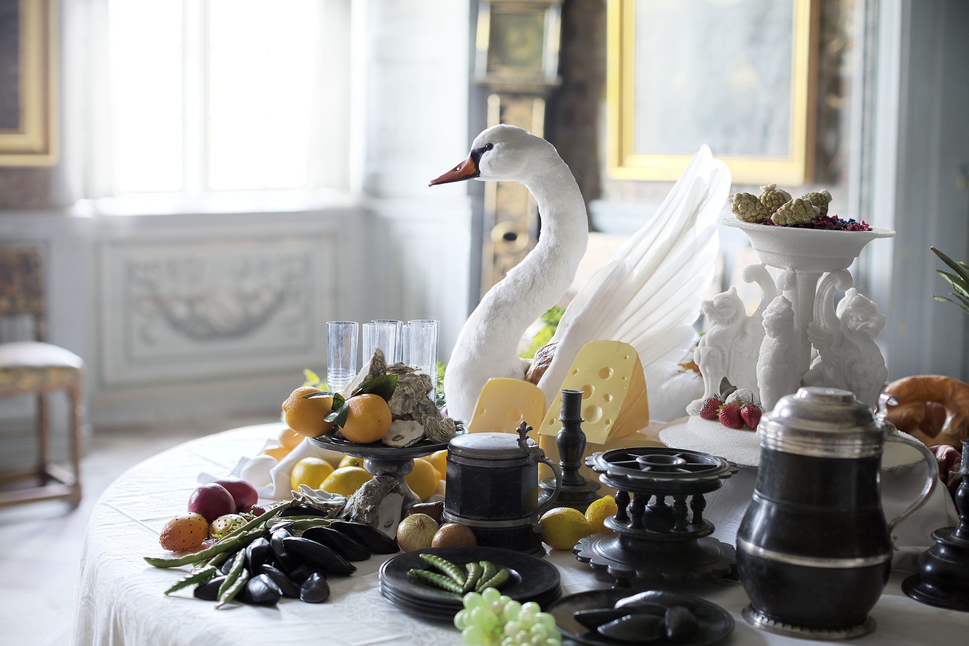  A table set with food, fruit and cheese. In the middle is a stuffed swan.