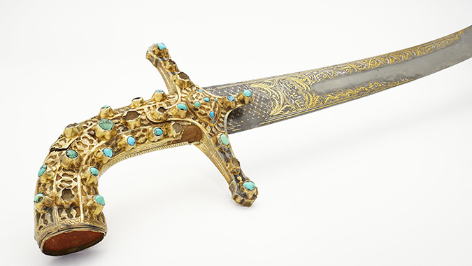 The grip of a sword. The handle is golden and studded with turquoise pearls.