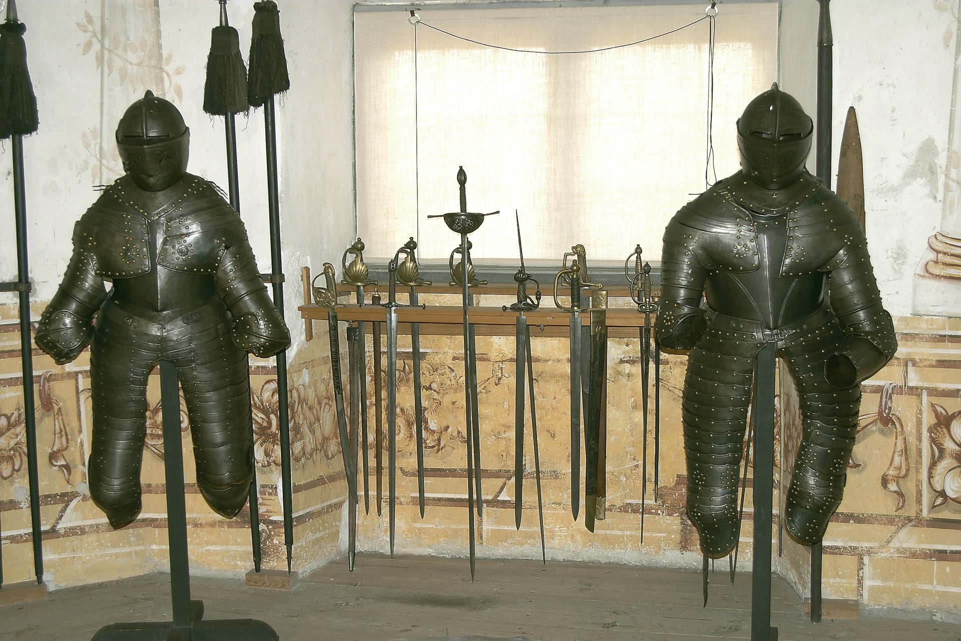 Two siuts of armour and some swords against a painted wall.