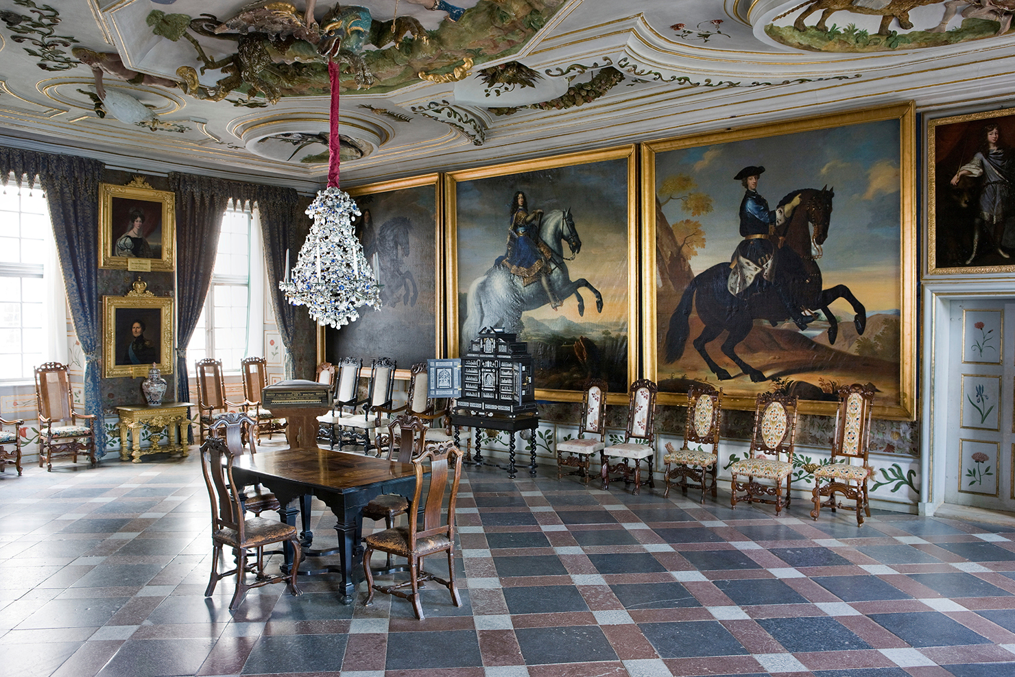 A large room with large paintings. The glass chandelier hangs from the ceiling.