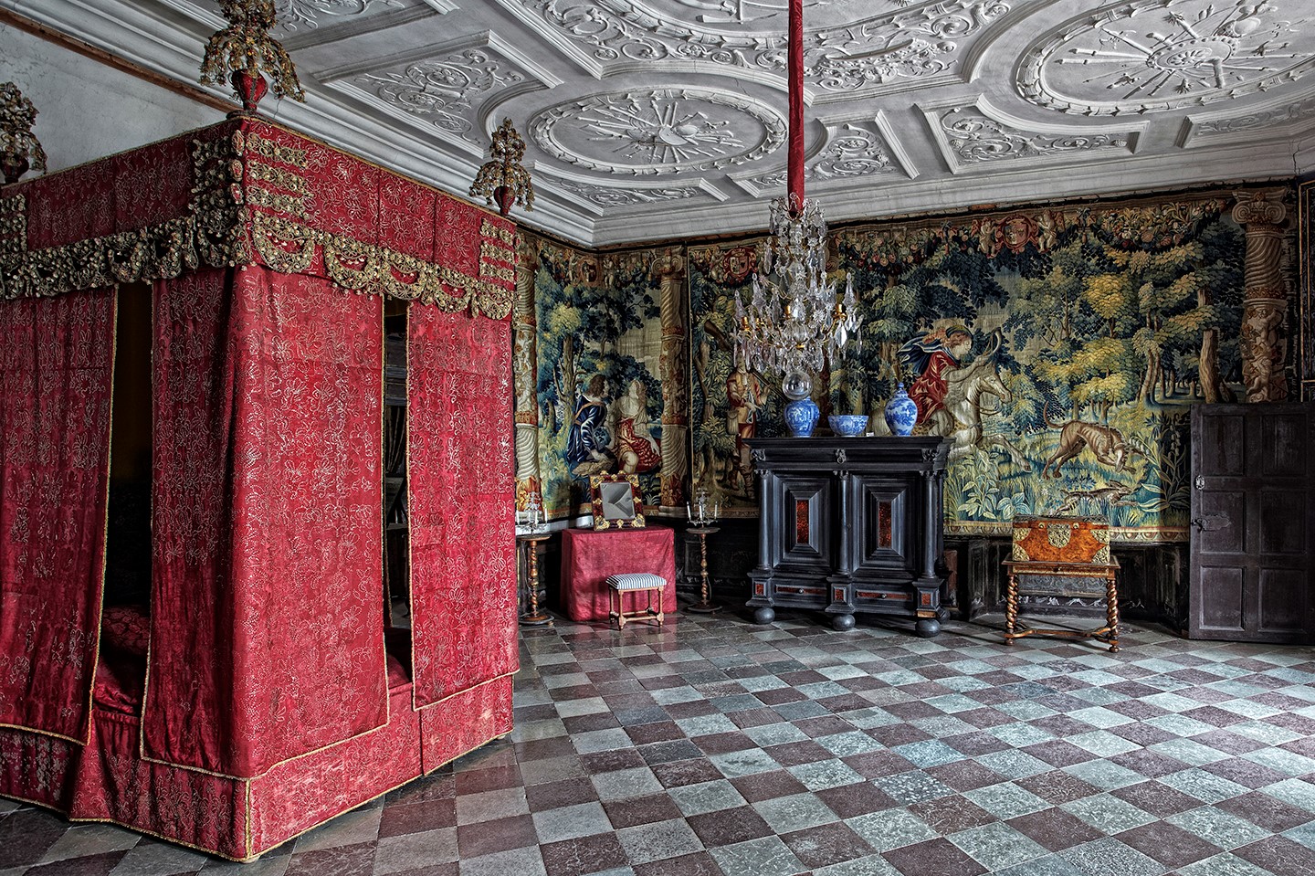 A large room decorated with tapestries, furniture and a large bed with red cover.