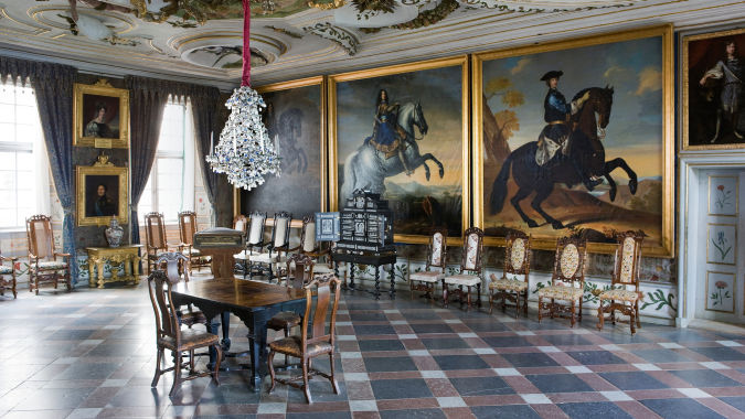 Bord och ljuskrona med stora målningar på väggarna i Kungssalen.