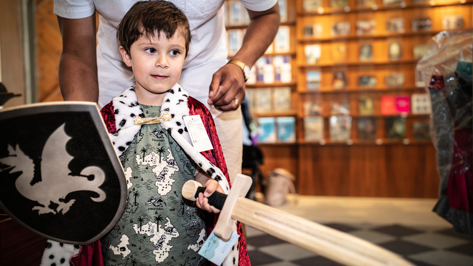 A child in the museum shop wearing a cloak and holding a toy sword.