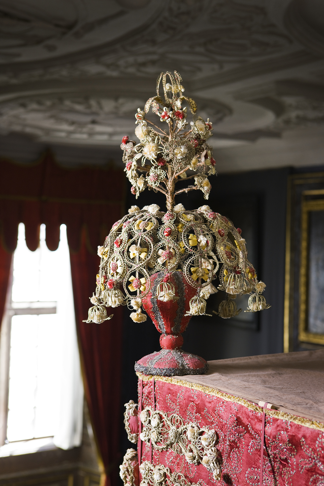 A pompom with turned base covered with red silk and topped with a buquet of white flowers made out of lace.