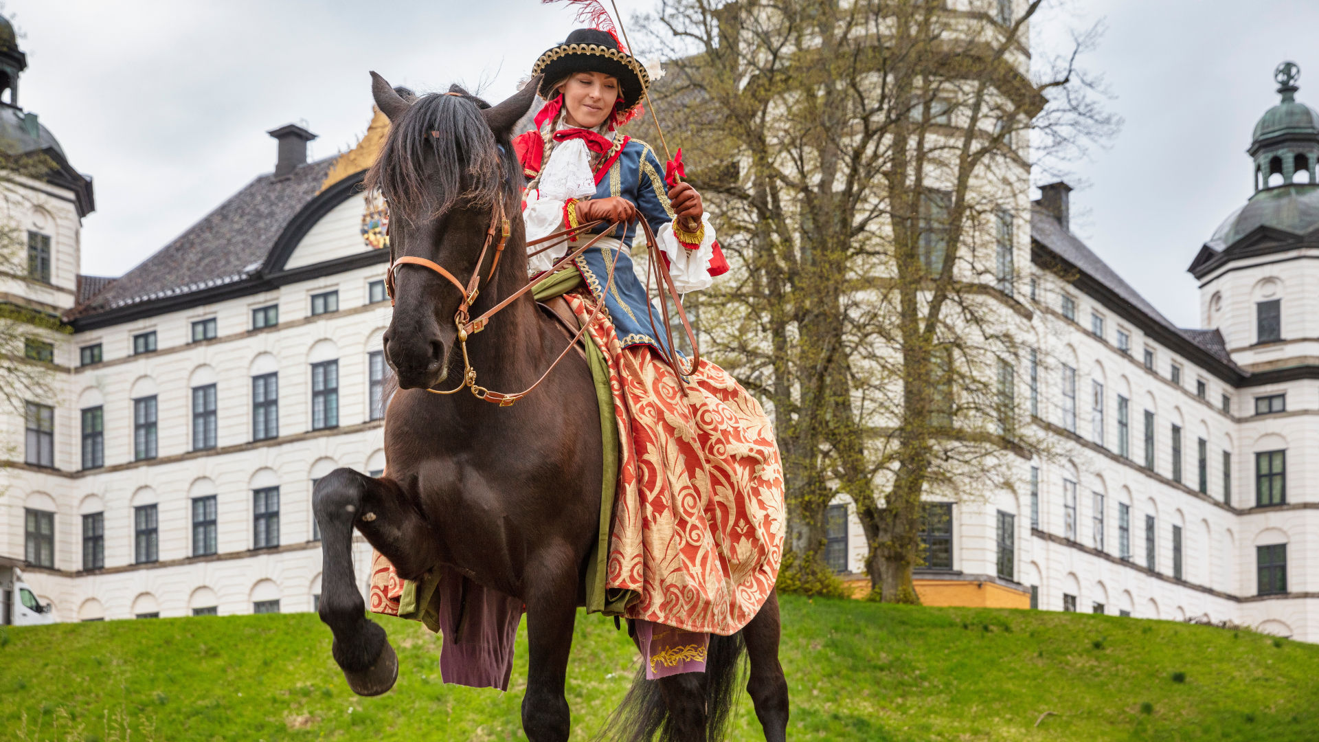  Rider in historical costume on brown horse in front of the castle.
