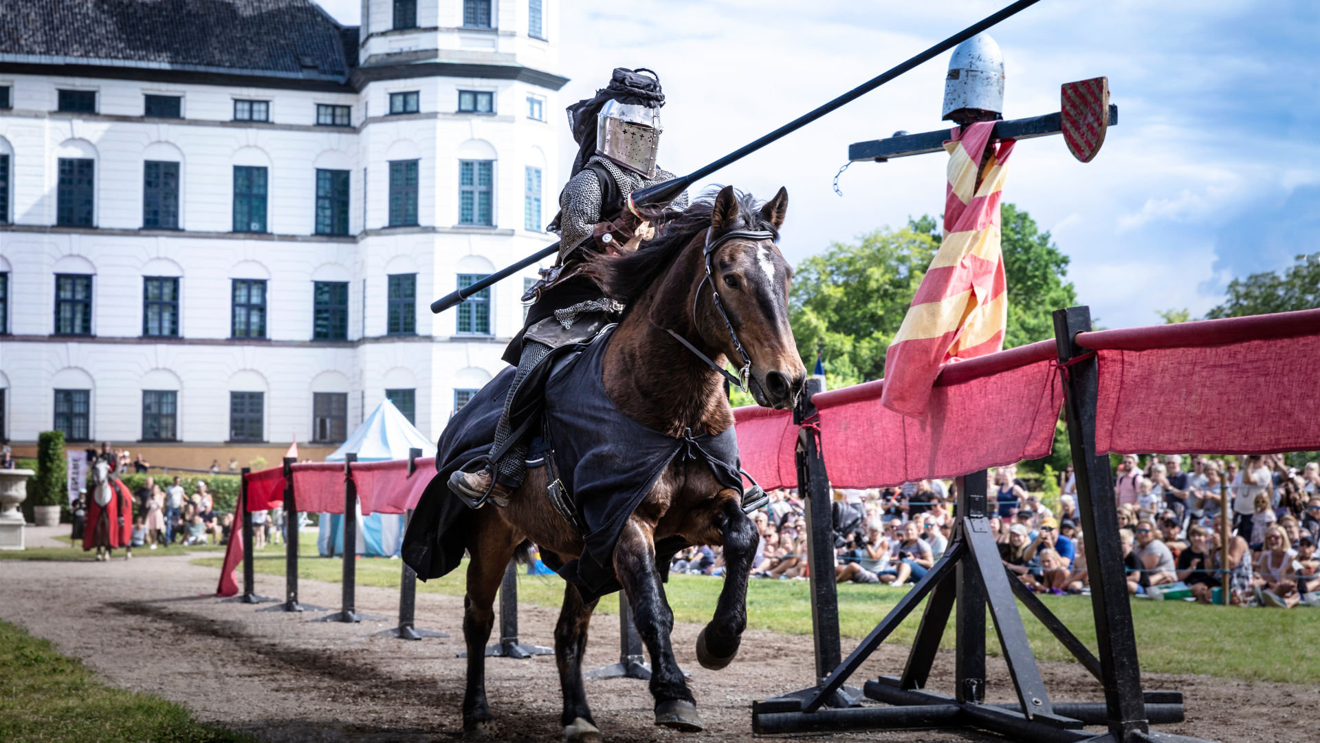 En person iklädd historisk rustning rider på häst framför slottet.