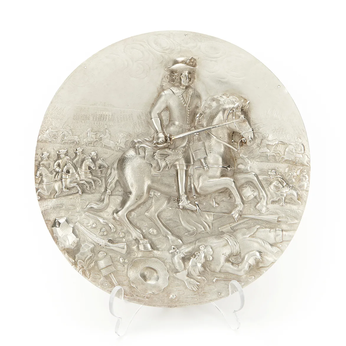 En rund silverskiva med en bild av en man till häst. Mannen har värjan dragen i höger hand. I bakgrunden rider andra män, inbegripna i en strid.
