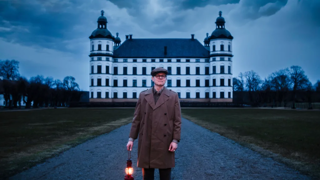 Man with lantern in front of castle with dark skies