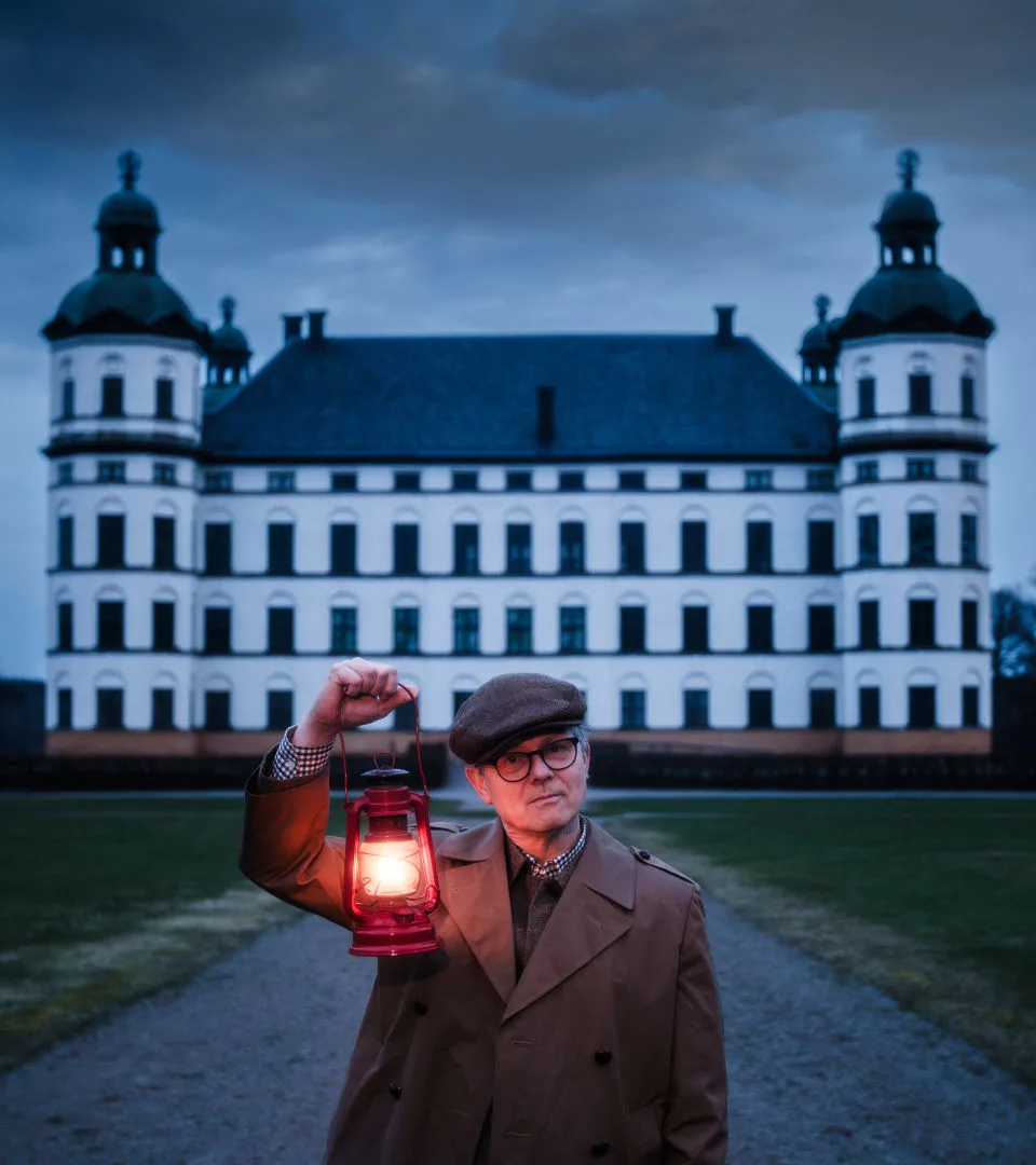 Man holding lantern in front of a dark castle