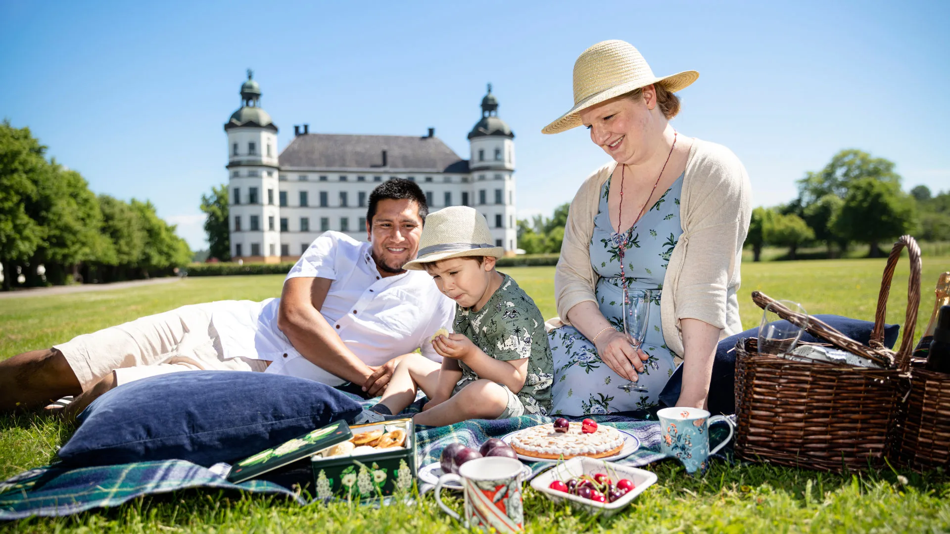 Bild på familj sittandes framför slottet på en picknik-filt med mat.